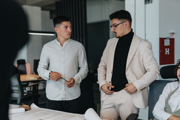 Multicultural business coworkers engaged in a collaborative discussion. Two men are focusing on analyzing documents and brainstorming project ideas in a contemporary workspace.