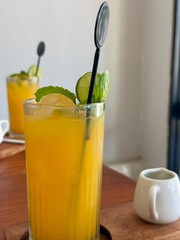 Fototapeta premium A glass of fresh orange juice with lime and mint on it. Juice on a wooden table in a cafe