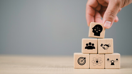 Hand placing wooden block with justice scale icon above teamwork and goal blocks, representing...