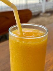A glass of fresh mango smoothie on a table in an outdoor cafe