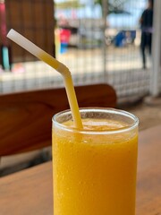 A glass of fresh mango smoothie on a table in an outdoor cafe
