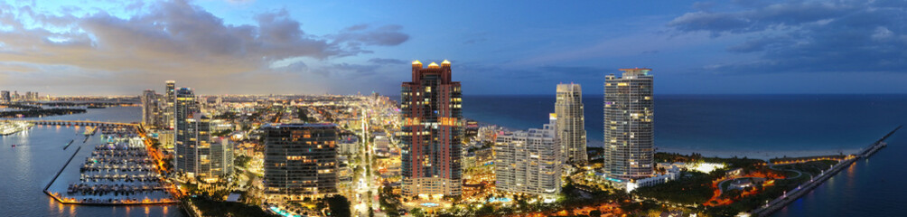 Aerial night view of Miami coastline. Twilight skyline above the Miami oceanfront. Miami Beach waterfront glowing after sunset. South Point lifeguard tower at dusk. Famous Miami Beach from above.