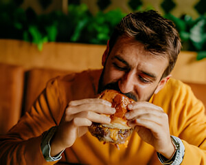 Burger Bite: A man relishes a hearty burger, showcasing the indulgence and pleasure of the moment.