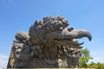 Fototapeta premium Magnificent Garuda Wisnu Kencana Cultural Park Stone Statue Captures Balinese Artistry and Religious Grandeur against a Clear Blue Sky, Showcasing Ancient Architectural Tradition and Heritage