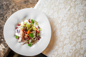 Fresh vegetable salad with cherry tomatoes, cranberries, parsley, and edible flowers on a white plate over floral-patterned tablecloth.