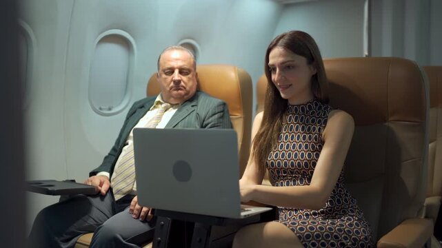 Western business class passengers, male and female, working or typing on a laptop while traveling on an airplane.