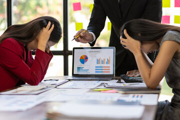 Angry manager scolding employees during business meeting. Businessman pointing at a laptop screen showing negative financial reports while scolding two frustrated female employees.
