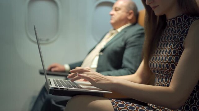 Western business class passengers, male and female, working or typing on a laptop while traveling on an airplane.
