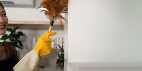 Home Cleaning. Woman using a feather duster to clean shelves with a smile.