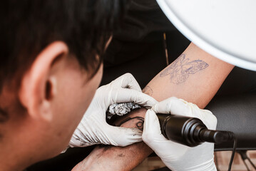 Tattooist uses rotary machine to draw bold black lines over stencil on forearm, creating tattoo...