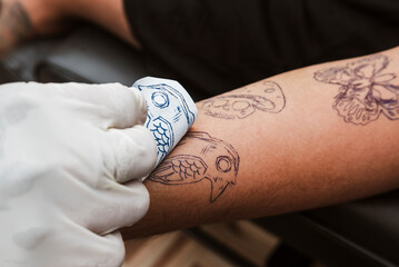 Tattoo artist peels off bird skull stencil paper from forearm, revealing the transferred ink...