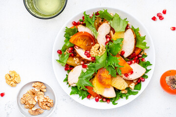 Yummy persimmon salad with grilled chicken, pomegranate, walnuts, oranges and lettuce, top view