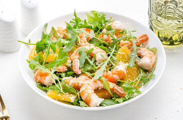 Seafood salad with juicy shrimps and orange, arugula and sesame on white background, top view