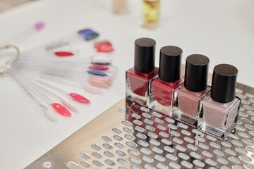 Four bottles of nail polish standing on metal tray near color palette samples arranged on table, showcasing variety of manicure options for beauty and nail care concepts
