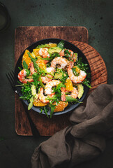 Gourmet seafood salad with shrimps, avocado, orange, arugula and sesame seeds on green stone background. Top view