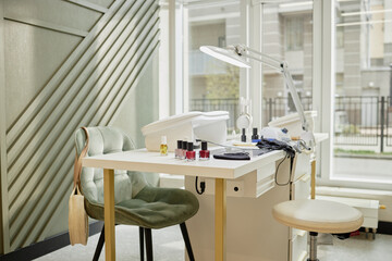 Modern manicure station featuring nail polish bottles, manicure tools, UV lamp and chairs positioned near large windows in bright professional nail salon interior