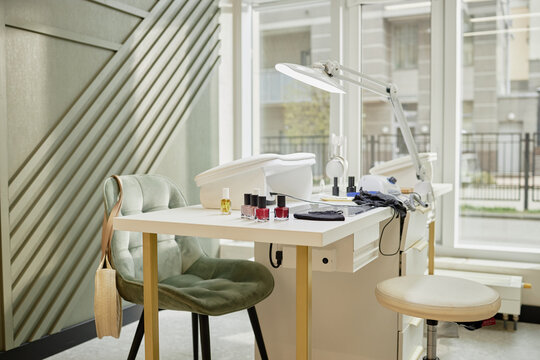 Modern manicure station featuring nail polish bottles, manicure tools, UV lamp and chairs positioned near large windows in bright professional nail salon interior