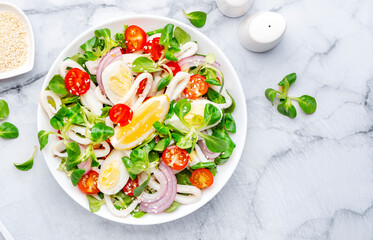 Seafood salad with squid, orange, tomatoes, lamb lettuce and olive oil with lemon juice dressing, gray table background, top view