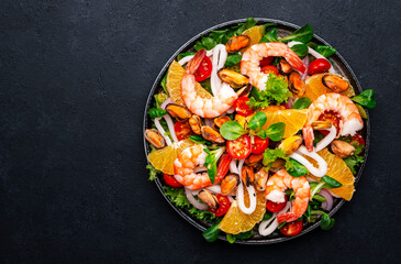 Delicious seafood salad with shrimp, mussels, squid, oranges, lettuce and olive oil with lemon dressing, black background, top view