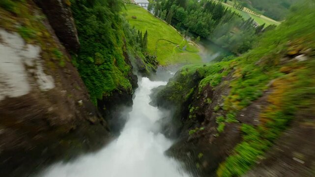 Aerial view of a powerful waterfall cascading down rugged cliffs into the Geirangerfjord, surrounded by lush greenery, Stranda Municipality, Norway.