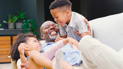 Grandfather Having Fun Playing With Grandchildren Sitting On Bench In Garden