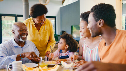 Family Shot With Grandparents Parents And Granddaughter At Breakfast Around Table At Home