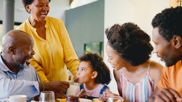 Family Shot With Grandparents Parents And Granddaughter At Breakfast Around Table At Home - Powered by Adobe