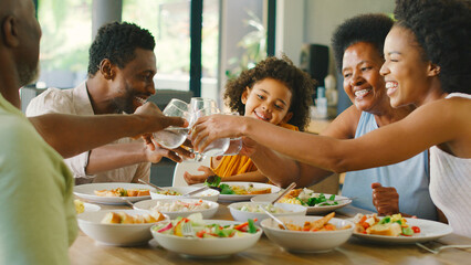 Naklejka premium Multi-Generation Family Around Table Doing Cheers With Water Before Serving Food For Meal At Home