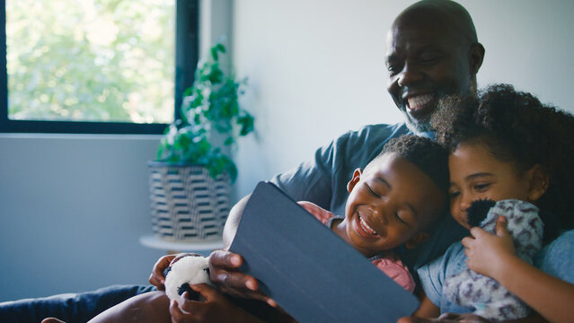 Grandfather With Grandchildren With Digital Tablet Sitting On Sofa Together Watching Movie Together