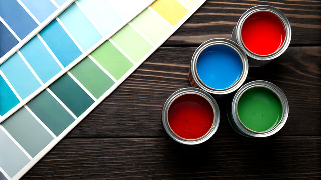 Vibrant paint cans and color swatches arranged on a rustic wooden surface for creative inspiration