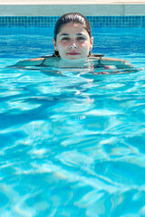 Young Woman Enjoying a Refreshing Swim in a Clear Blue Pool on a Sunny Day