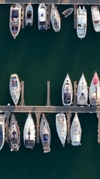 Top-down aerial view showing a marina with numerous yachts and boats neatly moored in parallel rows at sunset. 