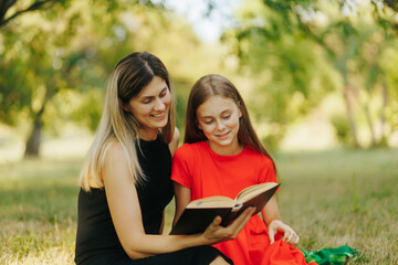 Naklejka premium Joyful mother and daughter reading barefoot in a grassy park