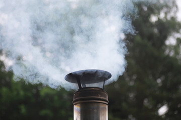 Outdoor Smoke Rising from Metal Chimney Against Blurred Forest Background