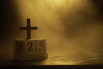 Wooden Cross and December 25 Calendar Block with Golden Backlight in Foggy Atmosphere