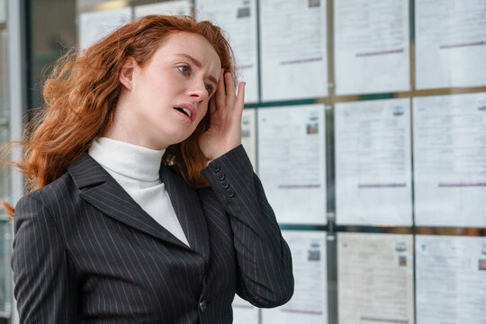 Businesswoman with red hair shows signs of stress while looking at job listings in a city office