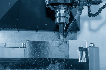 The CNC milling machine rough cutting the mold parts with oil coolant method in the blue tone scene.