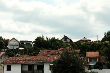 Traditional red-roof houses on a hillside in Serbia, surrounded by lush green trees under a cloudy sky.