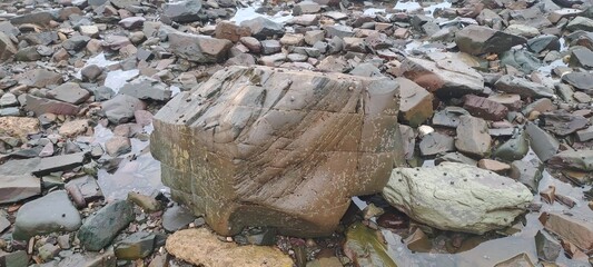 Large textured rock resembling a cube sitting on a rocky beach