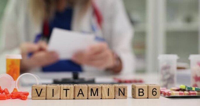 Wooden cubes spell word Vitamin B6 promoting healthy supplements while doctor works at desk. Pill packs stand near showing importance of vitamins
