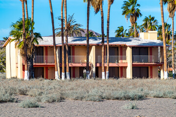 Abandoned apartment building in poor condition due to passage of time, among palm trees and dried wild plants, broken roof, sunny summer day in Loreto, Baja California Sur, Mexico