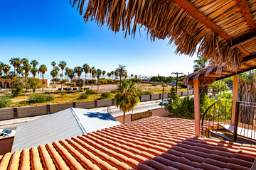 Beach landscape of coastal shore with abandoned tourist resort seen from a terrace, tiled roof, palm trees and wild vegetation, sunny spring day in Loreto, Baja California Sur, Mexico