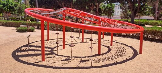 Red climbing dome structure casting shadow on playground sand in park