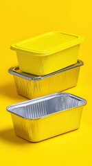 Stack of yellow and silver aluminum food containers on bright yellow background