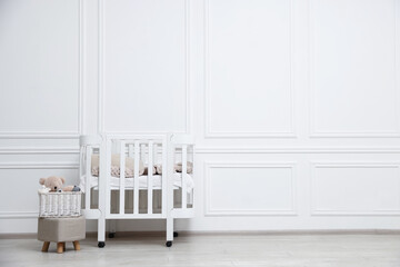 Fototapeta premium Comfortable crib, pouf and toys near white wall in baby's room, space for text. Interior design
