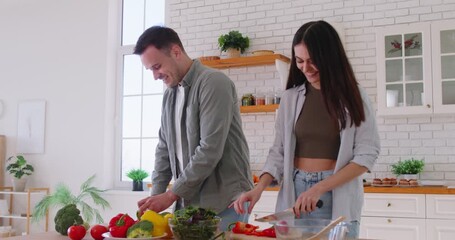Happy joyful funny young couple having fun dancing in kitchen preparing healthy salad with vegetables cooking at home together. Vegetarian food, diet and nutrition concept. 4k video. - Powered by Adobe