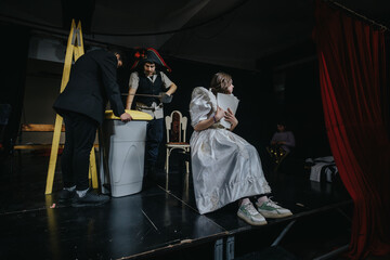 A group of young actors engaged in a theatrical rehearsal on stage, showcasing creative costumes and props, emphasizing the artistry of live performance.
