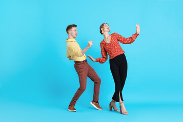 Naklejka premium Happy couple in retro outfits dancing on light blue background