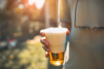 Person holding beer cup outdoors on a sunny day.
