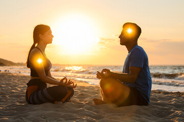 Couple meditating in Lotus pose on beach. Glowing bubbles representing chakras